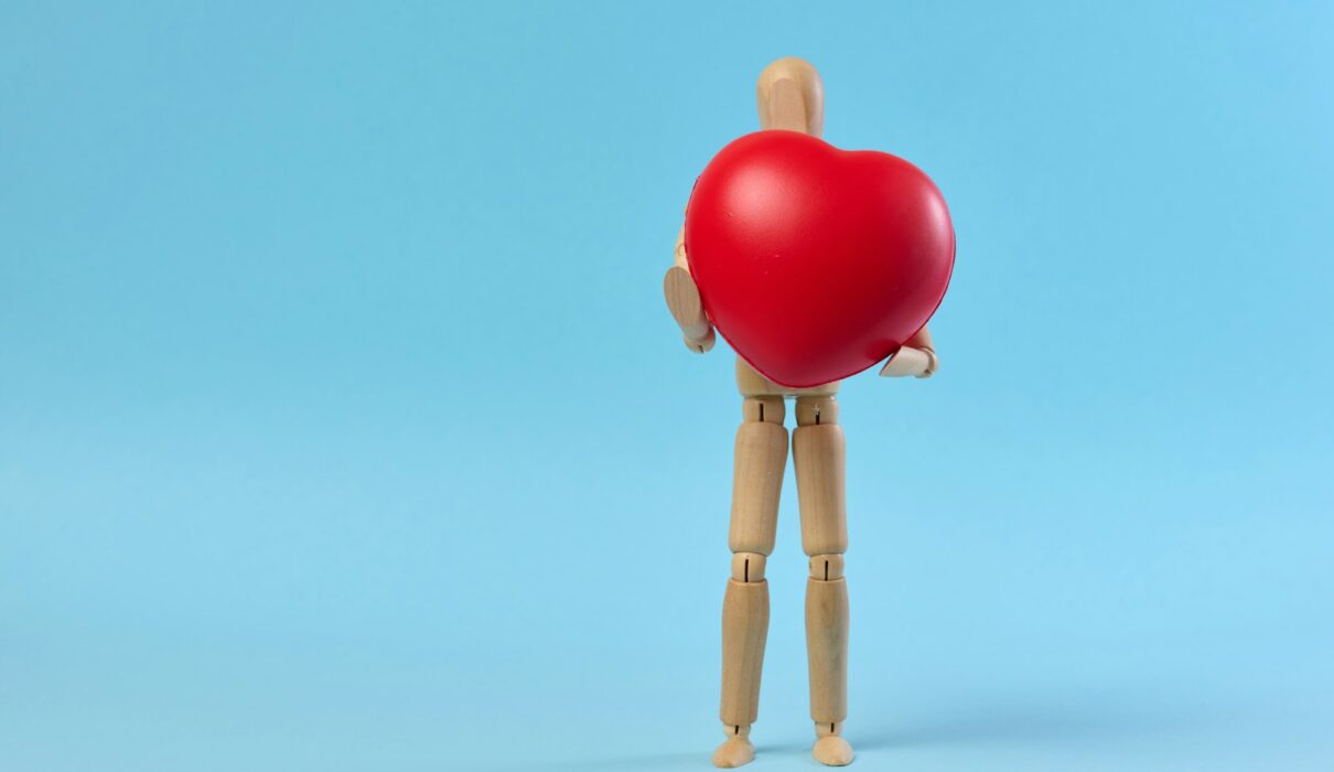 A wooden mannequin holding a red heart on a blue background, symbolizing the concept of blood