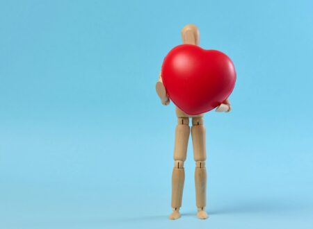 A wooden mannequin holding a red heart on a blue background, symbolizing the concept of blood