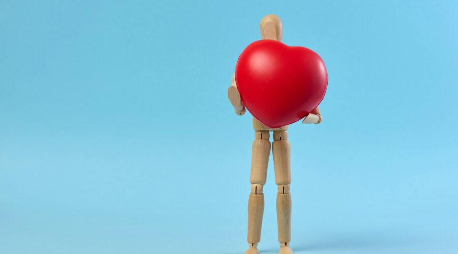 A wooden mannequin holding a red heart on a blue background, symbolizing the concept of blood