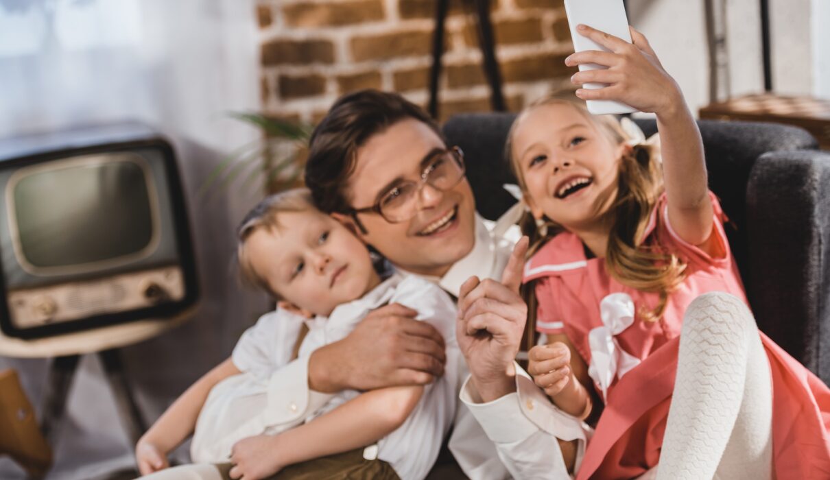 cheerful 1950s style family taking selfie with smartphone at home