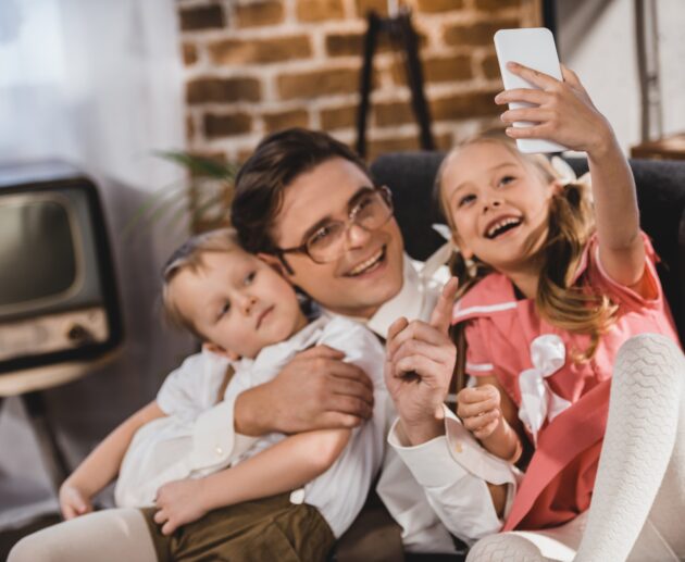 cheerful 1950s style family taking selfie with smartphone at home