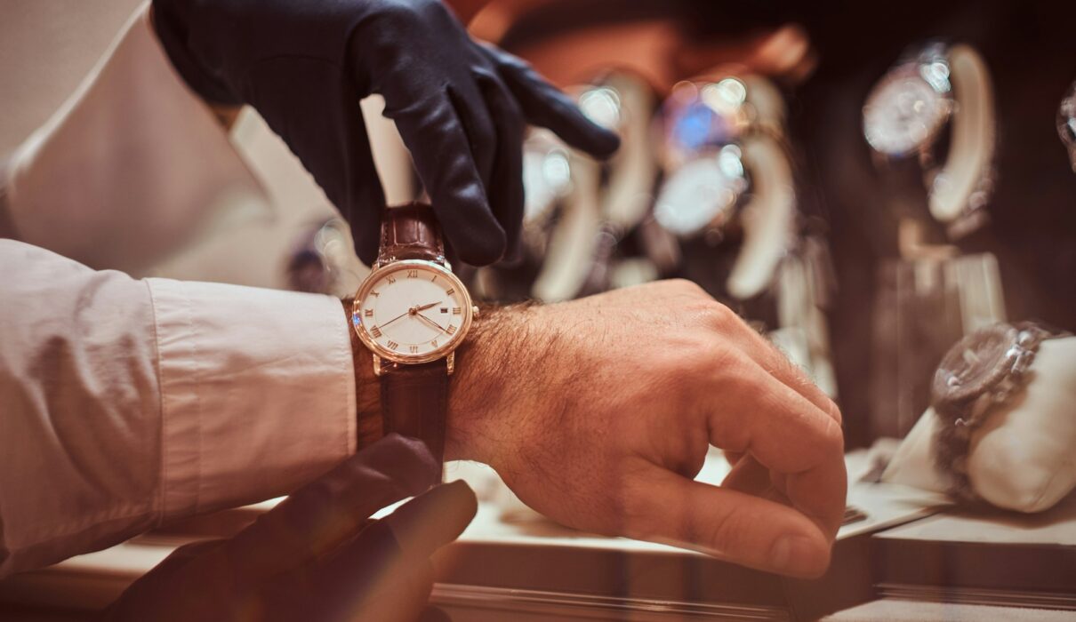 Close-up hands. Assistant helps the client to try on exclusive men's watches.