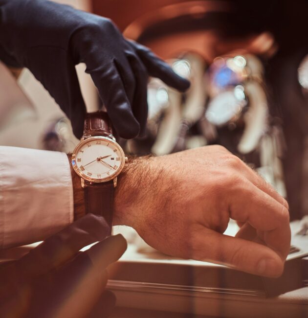 Close-up hands. Assistant helps the client to try on exclusive men's watches.