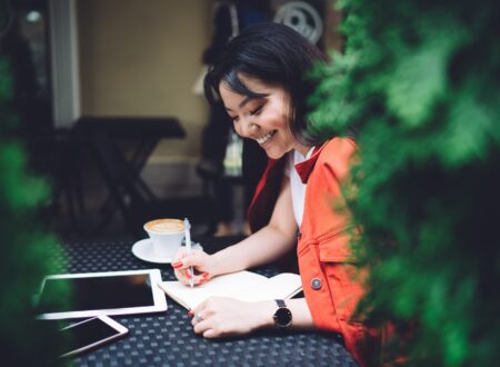 Excited ethnic woman writing down ideas in outdoor cafeteria