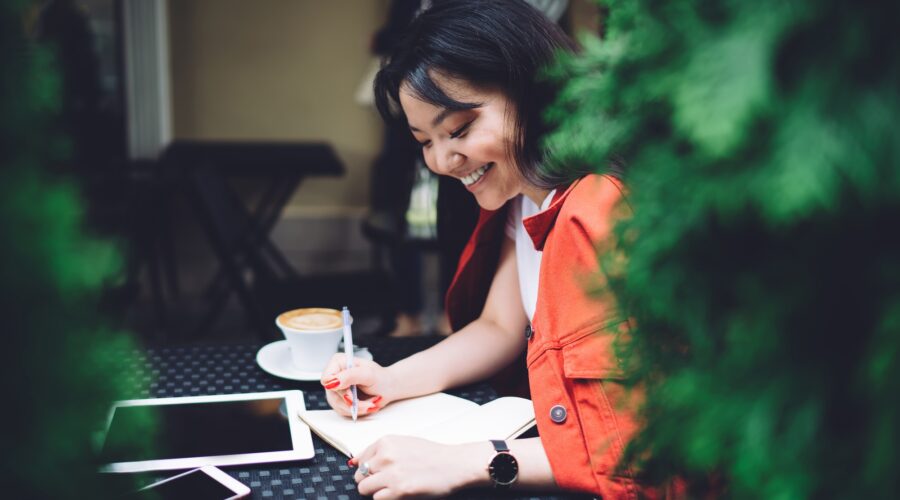 Excited ethnic woman writing down ideas in outdoor cafeteria