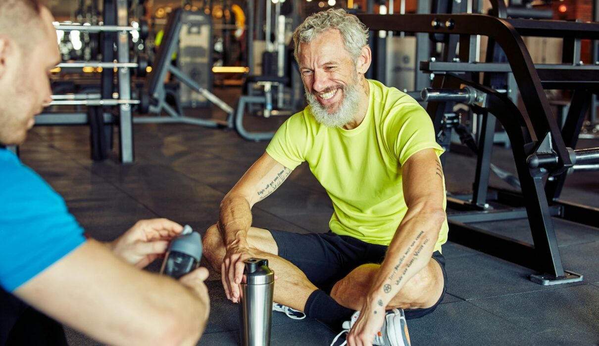 Exercising with personal trainer. Happy middle aged man discussing something with fitness