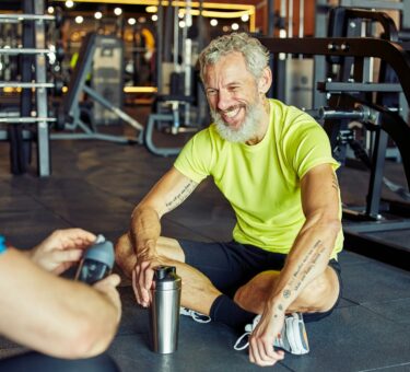 Exercising with personal trainer. Happy middle aged man discussing something with fitness