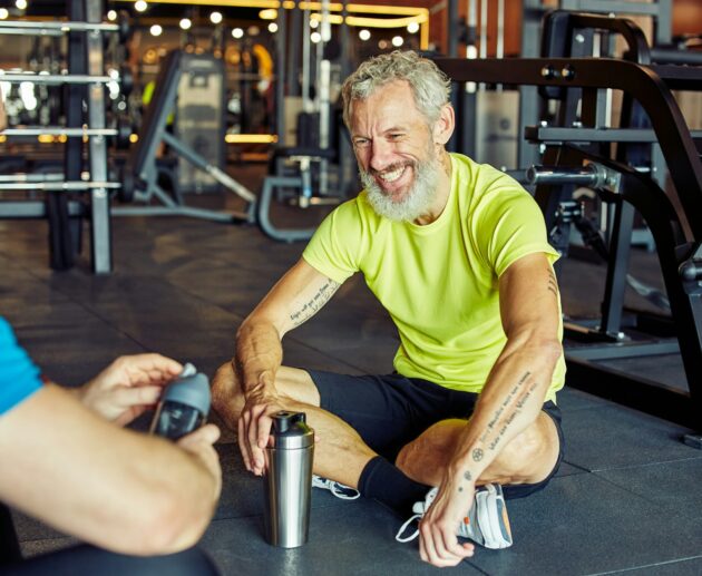 Exercising with personal trainer. Happy middle aged man discussing something with fitness