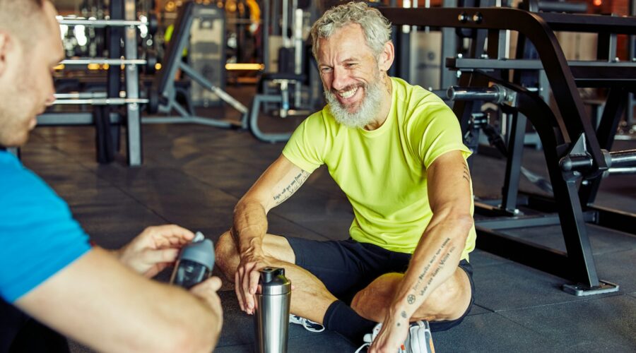 Exercising with personal trainer. Happy middle aged man discussing something with fitness