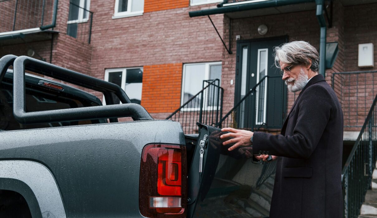 Fashionable senior man with gray hair and beard closes trunk of his car