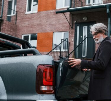 Fashionable senior man with gray hair and beard closes trunk of his car