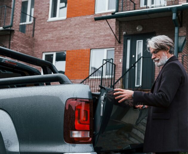 Fashionable senior man with gray hair and beard closes trunk of his car