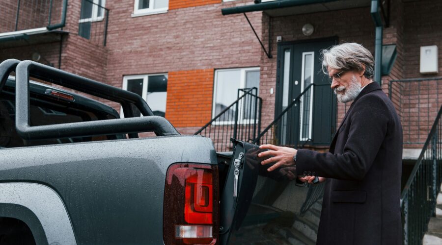 Fashionable senior man with gray hair and beard closes trunk of his car