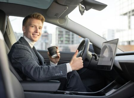 Handsome smiling Caucasian business man riding autonomous car, drinking coffee to go