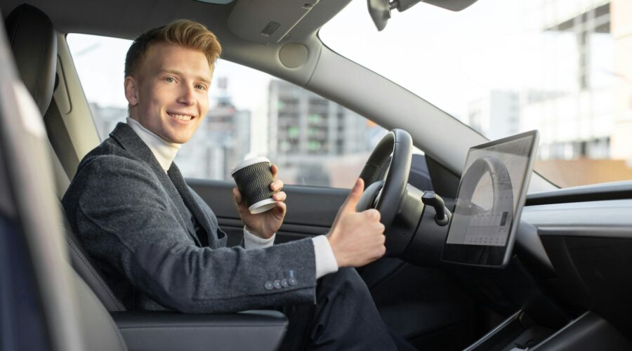 Handsome smiling Caucasian business man riding autonomous car, drinking coffee to go