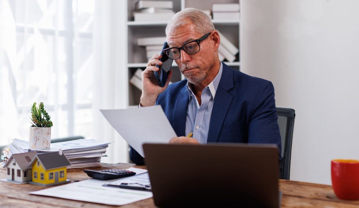 house model on workplace desk with real estate agent professional making business call talking on mo