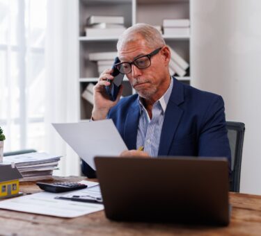 house model on workplace desk with real estate agent professional making business call talking on mo