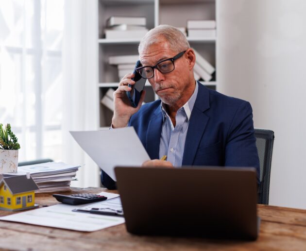 house model on workplace desk with real estate agent professional making business call talking on mo