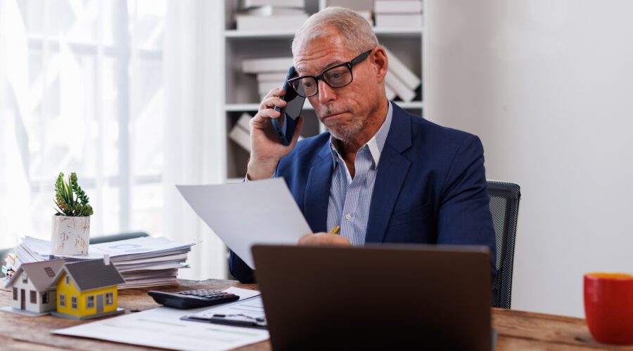 house model on workplace desk with real estate agent professional making business call talking on mo