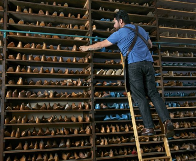 Male cobbler in traditional shoe shop on ladder selecting shoe last