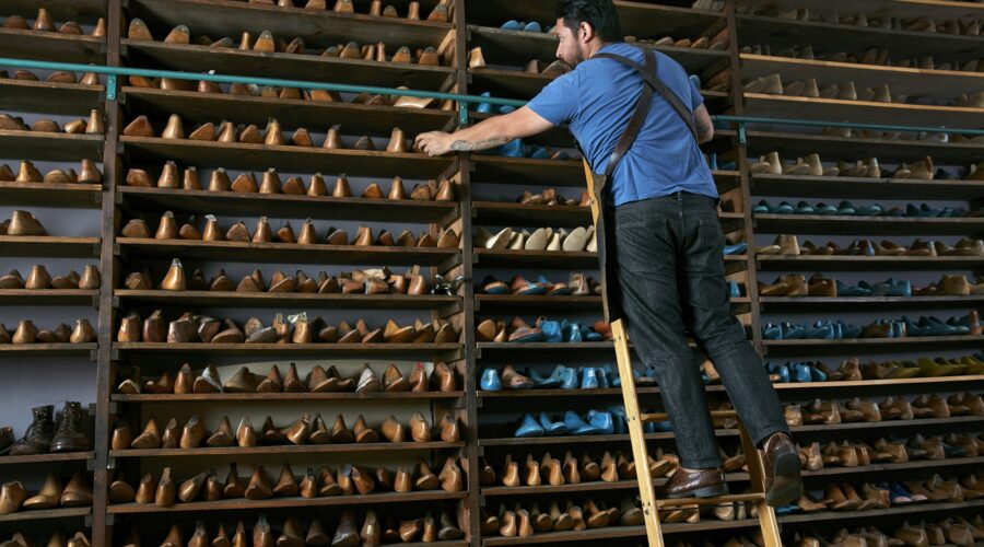 Male cobbler in traditional shoe shop on ladder selecting shoe last