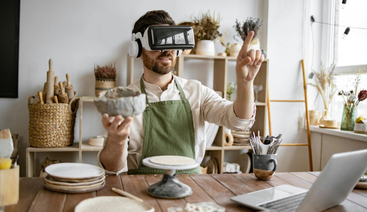 Man using virtual reality glasses to sculpt pottery in studio