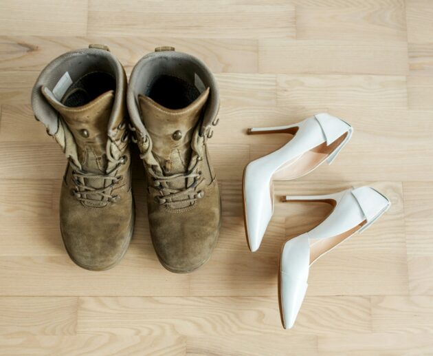 Old worn military boots, women's white shoes on wooden floor. Veteran and family concept.