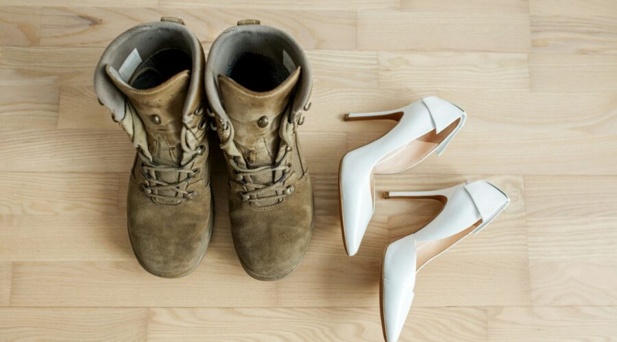 Old worn military boots, women's white shoes on wooden floor. Veteran and family concept.