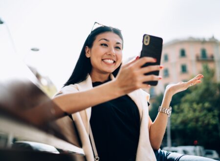 Overjoyed asian female in casual wear sitting on bench browsing information on smartphone via 4G