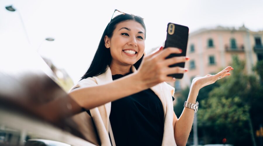 Overjoyed asian female in casual wear sitting on bench browsing information on smartphone via 4G