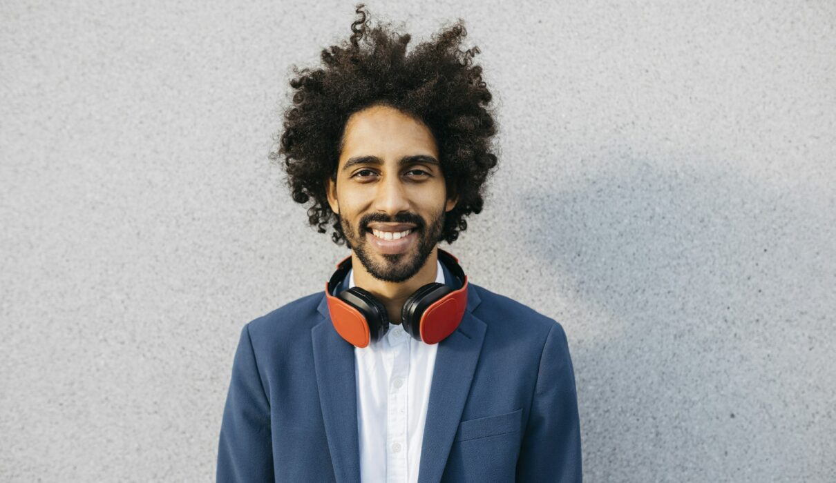 Portrait of smiling young businessman with headphones at a wall