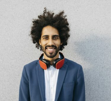 Portrait of smiling young businessman with headphones at a wall