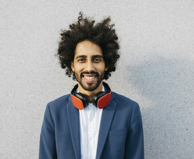 Portrait of smiling young businessman with headphones at a wall