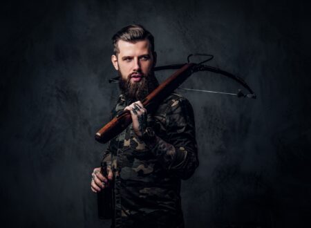 Stylish bearded hipster man in military shirt holding a craft beer and a medieval crossbow